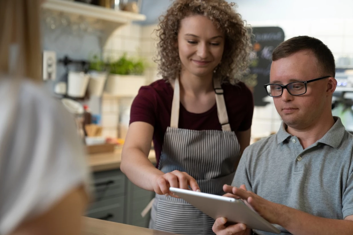 Support worker helping disabled man with down syndrome take customer order using iPad
