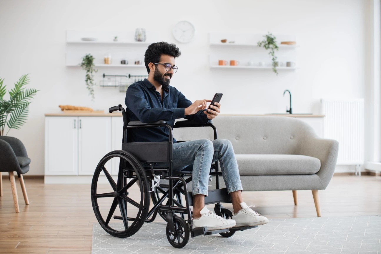 Disabled man in wheelchair sitting in living room using phone to make call
